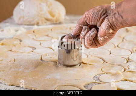 Schneiden von Kreisen aus Teig ein rundes Metallmesser. Zubereitung des Teigs zum Backen, ein großes Stück des Teigs liegt auf dem Tisch und der Koch schneidet Stockfoto