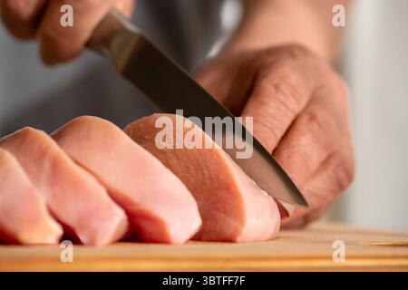hef Woman schneidet Hühnchen in der Küche. Die Köchin schneiden das Hähnchenfilet mit einem Messer. Hähnchenschneidtechnologie. Man schneidet Hühnchen mit Händen Stockfoto