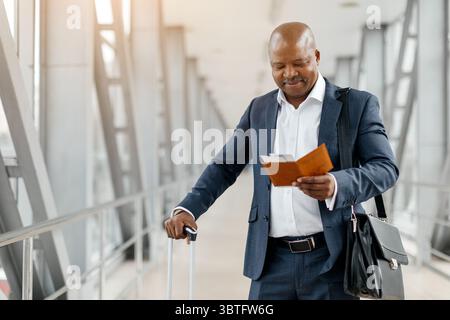 Schwarzer Geschäftsmann, der Koffer hält und Reisedokumente am Flughafen liest Stockfoto