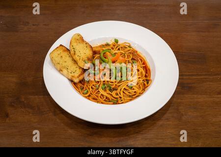 Spaghetti-Pasta in einer roten Tomatensauce, serviert mit zwei Scheiben Knoblauchbrot Stockfoto