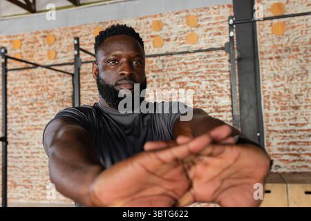 Afroamerikaner, der die Arme in Schulterhöhe im Fitnessstudio mit Pull-up-Rig und Plyometriekasten ausdehnt Stockfoto
