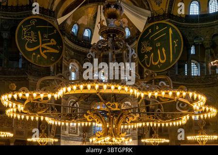 Das große Innere der Hagia Sophia Moschee in Istanbul, Türkei, mit seiner riesigen zentralen Kuppel, niedrigen Kronleuchtern und Kalligrafiemedaillon Stockfoto