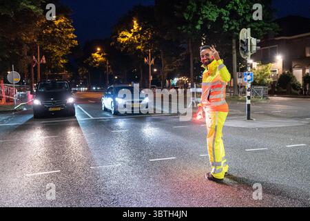 Nijmegen, Niederlande. Juli 2025. NIJMEGEN, NIEDERLANDE - 15. JULI: Tag 1 der vier-Tage-Märsche (Vierdaagse/4daagse), der weltweit größten mehrtägigen Wanderveranstaltung mit über 47,000 Teilnehmern. Verkehrssteuerung, die den Fluss der Wanderer lenkt, und regelmäßiger Autoverkehr lächelt zur Kamera. Am 15. Juli 2025 in Nijmegen, Niederlande. (Foto von John Beckmann/Orange Pictures) Credit: Orange Pics BV/Alamy Live News Stockfoto