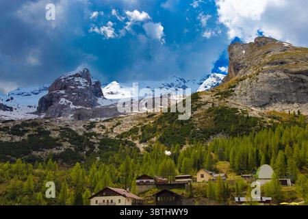 Die majestätischen schneebedeckten Gipfel der Marmolada überragen ein bezauberndes alpines Dorf inmitten üppiger grüner Wälder in den Dolomiten. Stockfoto