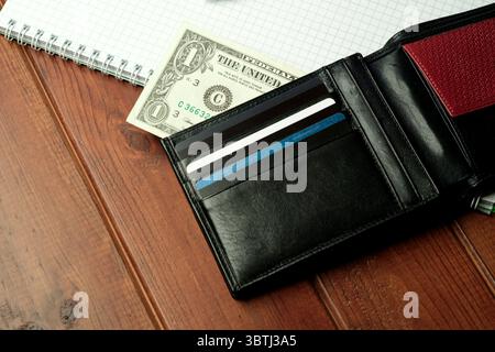 Eine elegante schwarze Geldbörse liegt auf einem Holztisch, in dem Bargeld und Karten im Inneren zu sehen sind. Stockfoto