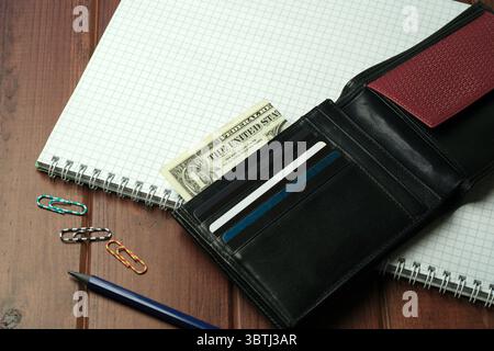 Eine schwarze Geldbörse zeigt Bargeld und Karten neben Spiralnotizbüchern und farbenfrohen Büroklammern. Stockfoto