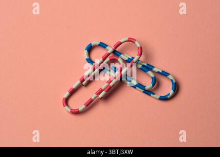 Bunte Büroklammern verflechten sich auf einer weichen Pastellfläche und schaffen Kunst. Stockfoto