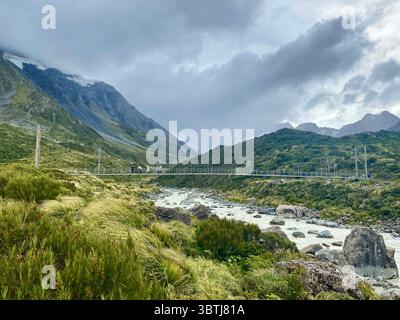 Hängebrücke über einen Gletscherfluss auf dem Hooker Valley Trail, Mount Cook National Park, Neuseeland, mit Wanderern und Berglandschaften unter Colos Stockfoto