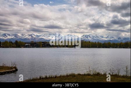 Anchorage, Alaska – 15. Mai 2024: Wolken über den Bergen hinter einem See mit einem Flugzeug, das an einem Frühlingstag in Anchorage landet. Stockfoto