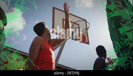 Springender Mann in rotem Panzertop, der auf dem Basketballfeld im Freien einen Korb erreicht, mit Basketball durch das Netz Stockfoto
