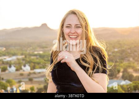 Eine Frau, die elegant in einem atemberaubenden schwarzen Kleid gekleidet ist, steht anmutig auf einem wunderschönen Hügel und lächelt hell vor Freude Stockfoto