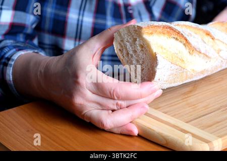 Hände einer älteren Frau, die geschnittenes Weißbrot in der Küche an einem braunen Tisch hält, ohne Gesicht, Nahaufnahme Stockfoto