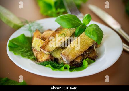 Hausgemachte gebratene Zucchini auf einem weißen Teller auf braunem Hintergrund. Stockfoto