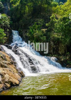 Ein ruhiger Abschnitt des Datanla Wasserfalls fließt über glatte Felsen in ein grünes Becken, umgeben von üppigem Grün und bewaldeten Klippen in da Lat Stockfoto