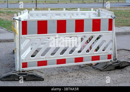 Warnzaun für einen kaputten Abschnitt der Straße, weißer und roter Kunststoffzaun, Stadtfotografie im Sommer an einem sonnigen Tag Nahaufnahme Stockfoto