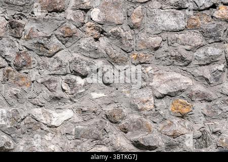 Hintergrund aus Steingranitmauerwerk mit Natursteinen, die hell von der Sonne beleuchtet werden Stockfoto