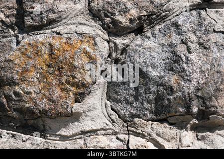 Hintergrund aus Steingranitmauerwerk mit Natursteinen, die hell von der Sonne beleuchtet werden Stockfoto