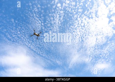 Drohne fliegend hoch im blauen Himmel mit verstreuten Wolken – Aerial Technology Concept mit Quadcopter in Aktion, von unten gegen einen wunderschönen Himmel gefangen Stockfoto
