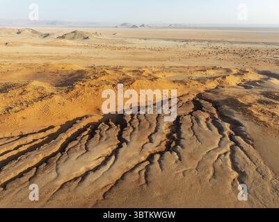 Aus der Vogelperspektive der trockenen Landschaft erschließt sich ein Wandteppich aus ockerfarbenen Dünen und rauer, skulpturaler Erde unter einem riesigen Himmel, Tsondab Valley, Khomas, Namibia. Stockfoto