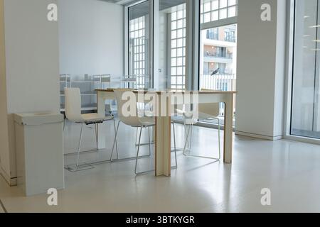 Es gibt einen Schreibtisch in der Mitte des Zimmers. Ein geräumiges Büro mit großen Fenstern und weißen Wänden. Minimalistischer Büroinnenraum. Stockfoto