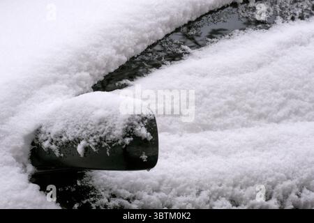 Dunkler Pkw auf einem schneebedeckten Parkplatz in der Stadt an einem bewölkten Wintertag Stockfoto