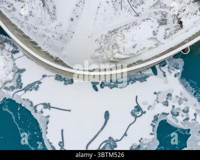 Aus der Vogelperspektive eines Damms, der das türkisfarbene Wasser vom schneebedeckten Land trennt und einen starken Kontrast zwischen den Elementen schafft, Anniviers, Wallis, Schweiz. Stockfoto