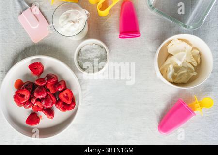 Blick über die Zutaten und Utensilien für die Zubereitung von hausgemachtem Eis mit Erdbeeren, Hüttenkäse und Sahne Stockfoto