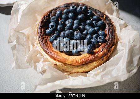 Nahaufnahme eines verbrannten baskischen Käsekuchens mit frischen Heidelbeeren und Kuchenscheiben auf Tellern Stockfoto