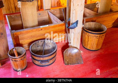 Das Innere einer alten Wassermühle mit Holzeimern, Schaufel und rotem Boden Stockfoto