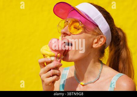 Lebhaftes Porträt einer jungen Frau, die an einem heißen Tag im Freien in hellem Sommersonnenlicht schmelzendes Eis isst Stockfoto