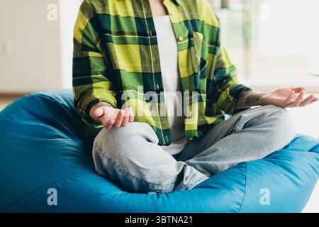 Junge Frau, die zu Hause in bequemer, ungezwungener Art meditiert, auf Sitzsack sitzend, friedliche Gedankenübungen in Innenräumen annimmt Stockfoto