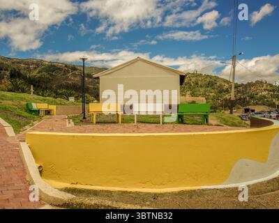 Drei Parkbänke aus Beton in verschiedenen Farben, von vorne gesehen hinter einer großen gelben runden Mauer, in einem öffentlichen Raum in der Stadt Sora, in der an Stockfoto