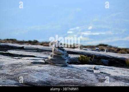 Ein sorgfältig ausbalancierter Stein steht auf felsigem Gelände am Mount Kinabalu, umgeben von karger Vegetation und unter einem trüben blauen Himmel Stockfoto