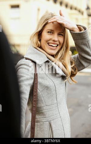 Porträt einer glücklichen, schönen blonden Frau im Wollmantel auf dem Bürgersteig Stockfoto