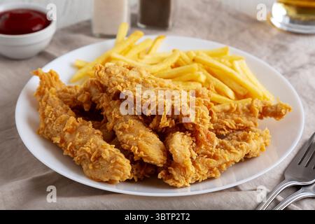 Hausgemachte Hähnchenstreifen mit Pommes frites auf einem Teller, Blick aus einem niedrigen Winkel. Nahaufnahme. Stockfoto