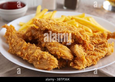 Hausgemachte Hähnchenstreifen mit Pommes frites auf einem Teller, Blick aus einem niedrigen Winkel. Nahaufnahme. Stockfoto