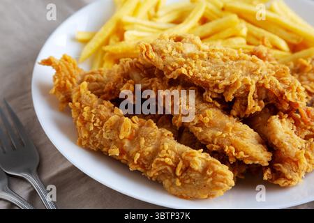 Hausgemachte Hähnchenstreifen mit Pommes frites auf einem Teller, Blick aus einem niedrigen Winkel. Nahaufnahme. Stockfoto