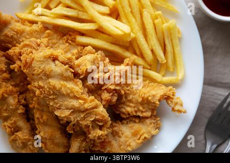 Hausgemachte Hähnchenstreifen mit Pommes frites auf einem Teller, Draufsicht. Stockfoto