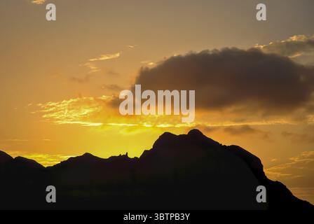 Silhouette des Bergrückens bei Sonnenuntergang mit goldenem Himmel und dramatischen Wolken. Stockfoto