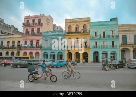Farbenfrohe Kolonialgebäude im Zentrum von Havanna, Kuba. Menschen, Fahrräder und Oldtimer vor den pastellfarbenen Fassaden in einer belebten Stadtstraße. Stockfoto