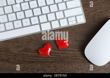 Dekorative Herzen, Computertastatur und Maus auf Holztisch, flach gelegen. Online-Dating-Website Stockfoto