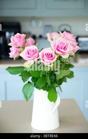 Einfache Kanne, die als Vase für eine Ausstellung von rosa Rosen in einer Landhausküche, England, verwendet wird Stockfoto