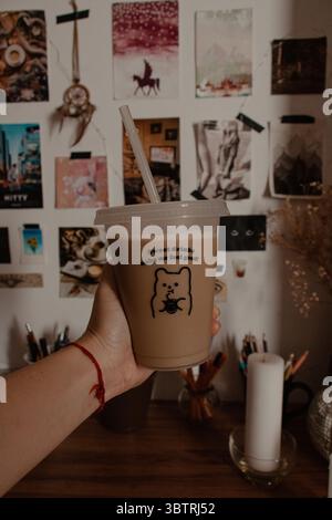 Hand hält eiskalte Kaffeetasse im Zimmer Stockfoto