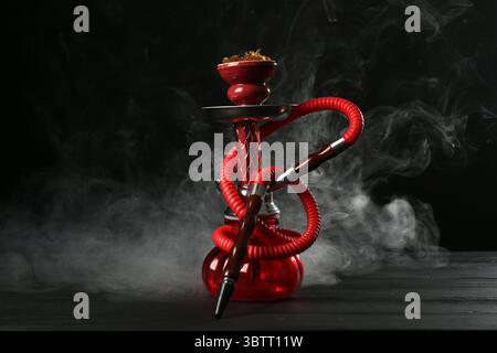 Shisha auf Holztisch mit Rauch vor schwarzem Hintergrund Stockfoto