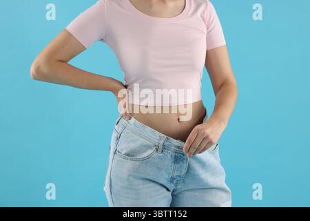 Frau trägt alte Jeans nach Gewichtsverlust auf hellblauem Hintergrund, Nahaufnahme Stockfoto