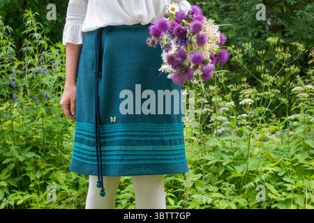 Weite Landschaftsansicht einer Person in einem Garten, umgeben von üppigem Grün, mit einem Blumenstrauß und in sanftem natürlichem Licht – eine ruhige rura Stockfoto
