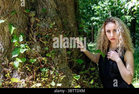 Ein wunderschönes blondes moldauisches Model posiert an einem sonnigen Julitag unter Baumkronen im Dundee Camperdown Country Park in Schottland, Großbritannien Stockfoto