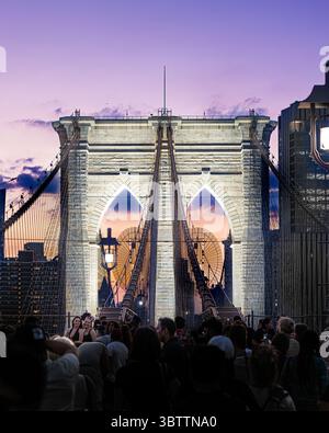 Brooklyn Bridge Fußgänger, die bei Sonnenuntergang am Abend und in der Nacht spazieren gehen, sehen Sie die Kabel und Steinbögen in Lower Manhattan, New York City Stockfoto