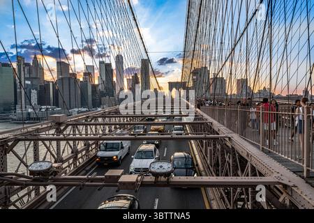 Brooklyn Bridge Traffic - Autos bei Sonnenuntergang Abend und Nacht Herbst - Nahaufnahme von Kabeln und Steinbögen in Lower Manhattan New York City Stockfoto