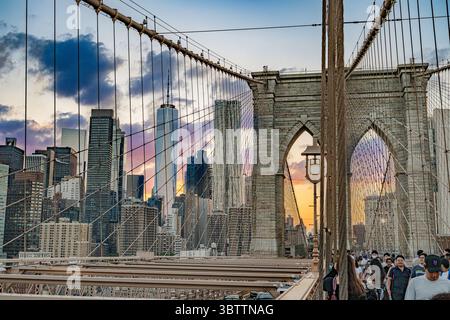 Brooklyn Bridge Fußgänger, die bei Sonnenuntergang am Abend und in der Nacht spazieren gehen, sehen Sie die Kabel und Steinbögen in Lower Manhattan, New York City Stockfoto